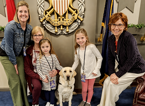 Dr. Carolann Wolfgang and her family pose together in the Joint Chiefs of Staff Flag Room at the Pentagon.