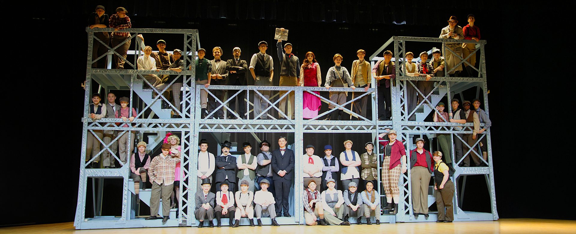 North Schuylkill students perform Newsies on a large multi-level stage set, posing in period costumes during a full-cast scene.