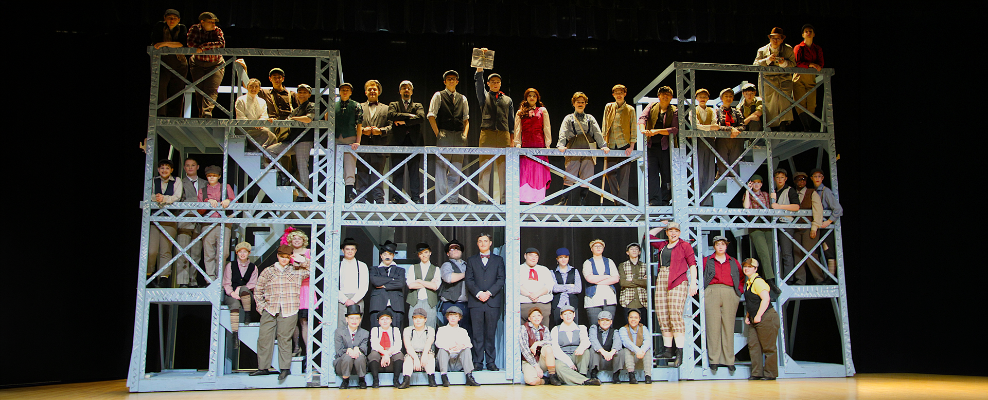 North Schuylkill students perform Newsies on a large multi-level stage set, posing in period costumes during a full-cast scene.