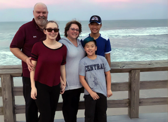 Amy Brayford poses with her husband Fran and their three children in an outdoor family portrait.