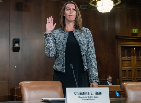 Judge Christina E. Hale raises her right hand to take the oath of office in a courtroom, with her nameplate reading Magisterial District Judge, Schuylkill County visible in the foreground.