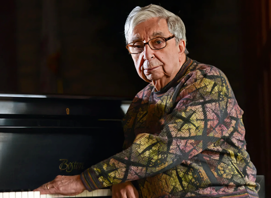Dr. Robert Mulligan, radiologist and trombonist, seated at a piano in a reflective portrait.
