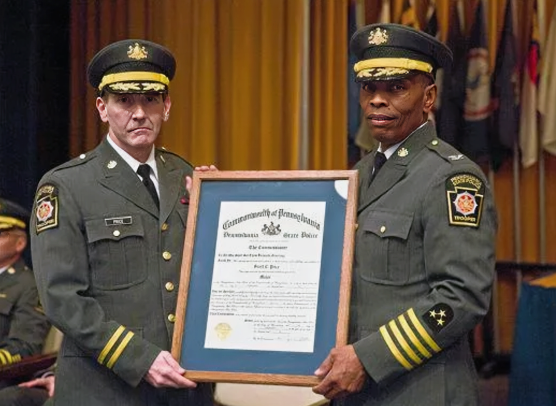 Lt. Colonel Scott C. Price in full Pennsylvania State Police dress uniform, holding a ceremonial certificate alongside a fellow officer during a formal recognition event.