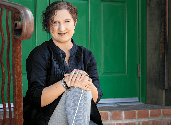 Dr. Angelica Dunsavage, choral conductor and professor, seated outdoors holding a conductor's baton.