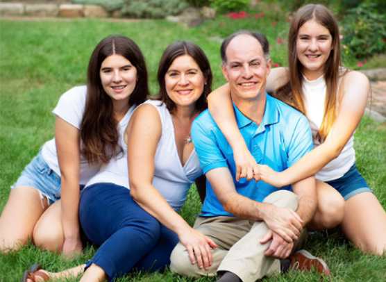 Dr. Rebecca Zarutskie poses with her husband and two daughters in a casual outdoor family portrait.